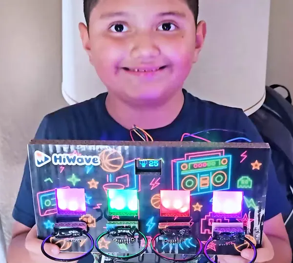 A young maker holding the light-up hoops game he built, its four targets glowing